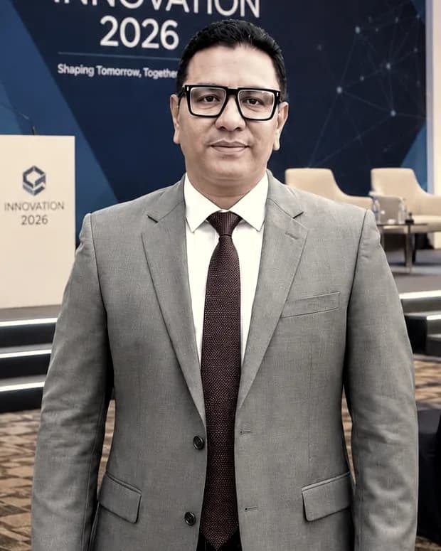 Rahul Joshi in a grey suit in front of a lit conference stage and branded backdrop.