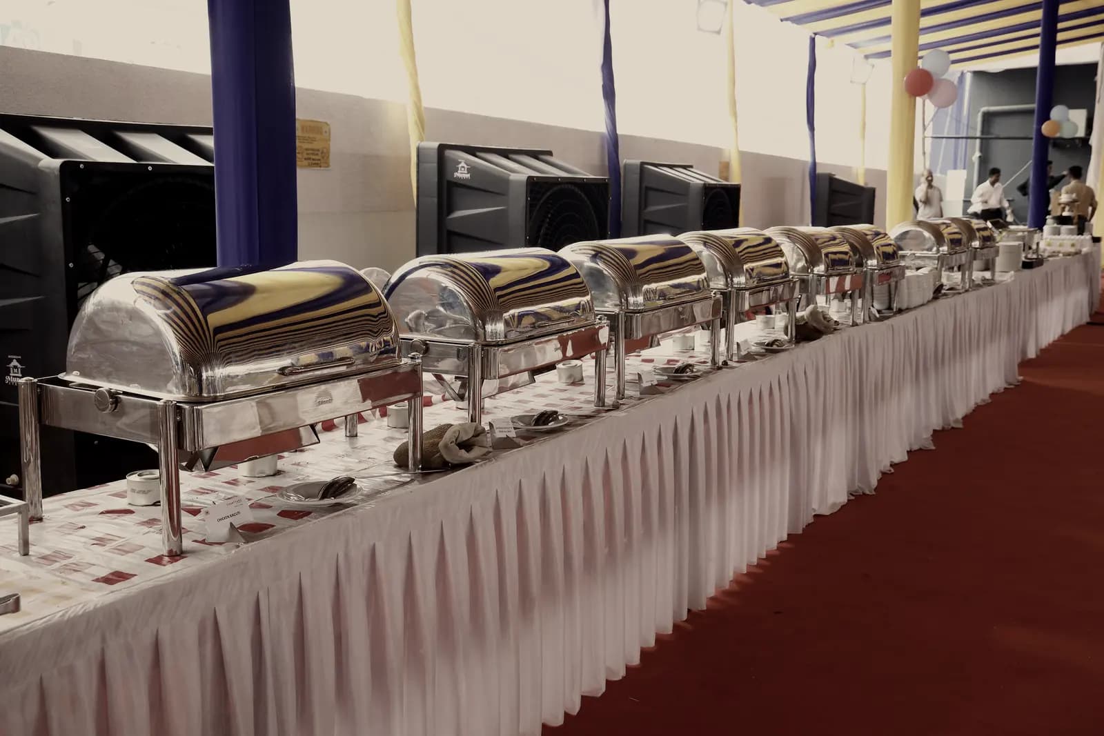 A long buffet run of chafing dishes stretching down a skirted table under drapes.