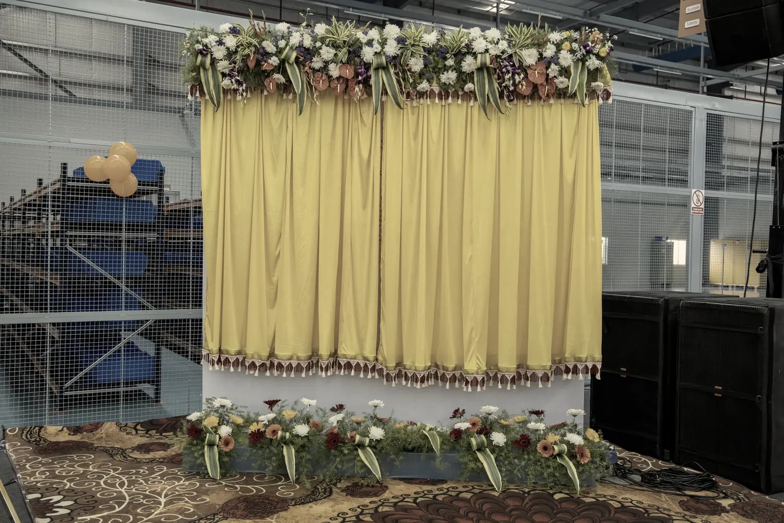 A ceremony backdrop of gathered fabric topped with a full band of fresh flowers, flowers along its base.