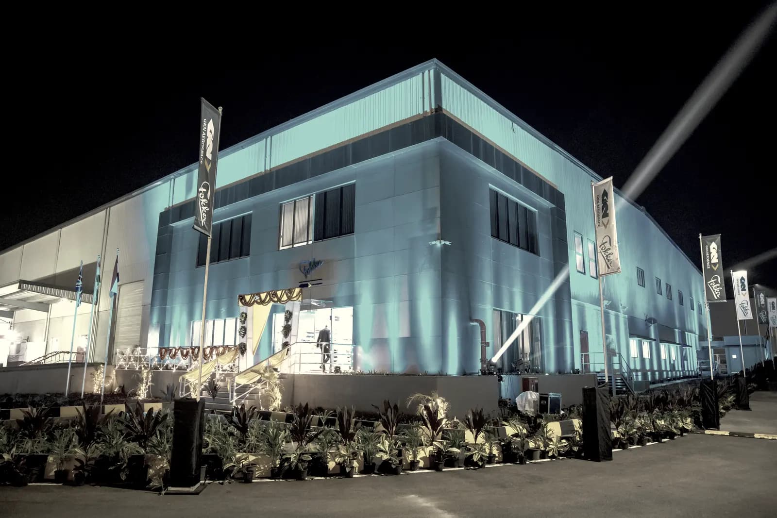 The same building lit in cobalt blue later in the evening, flag banners along the entrance path.
