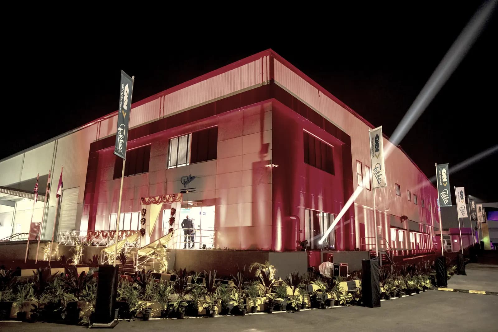 A factory building washed end to end in deep red architectural light, beams crossing the sky above it.