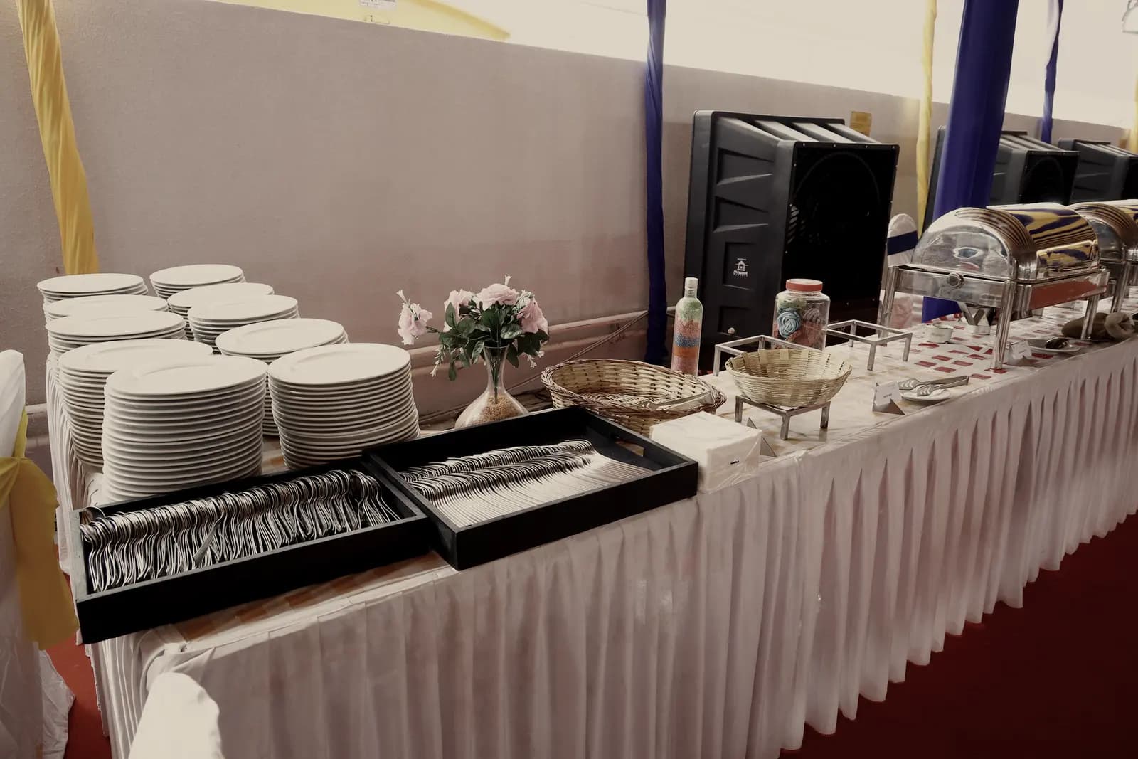 Stacked plates, rolled cutlery trays and a small flower arrangement at the head of a service table.