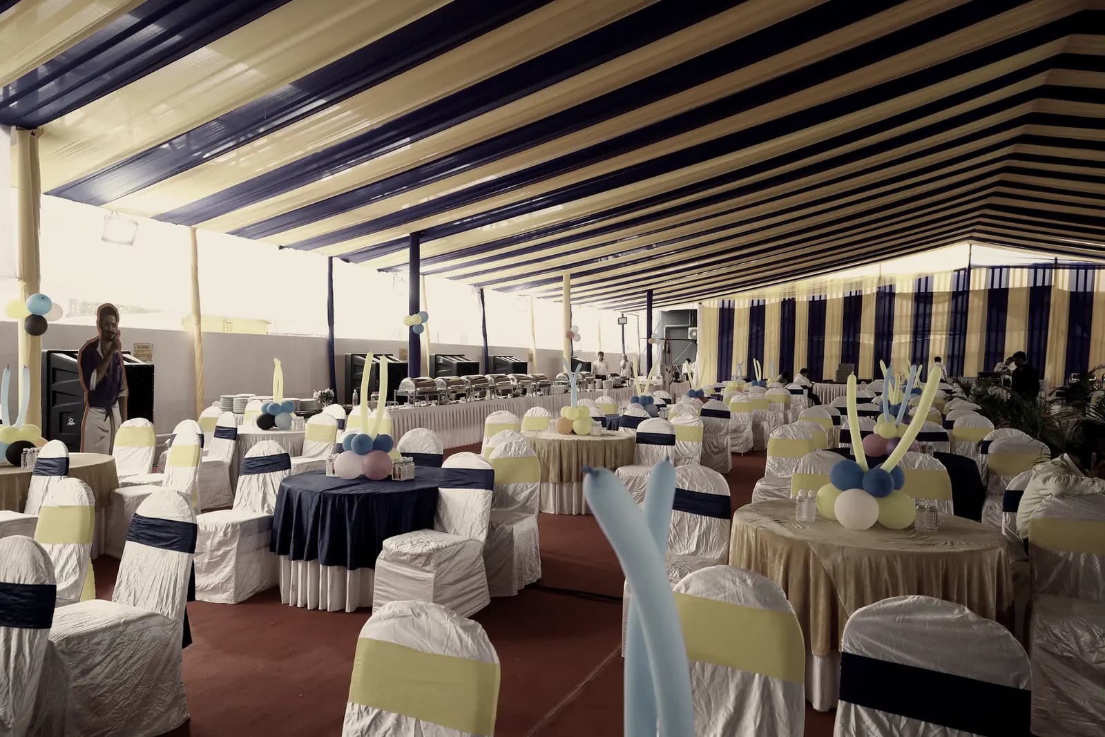 A striped marquee over round banquet tables dressed and set, before guests arrive.