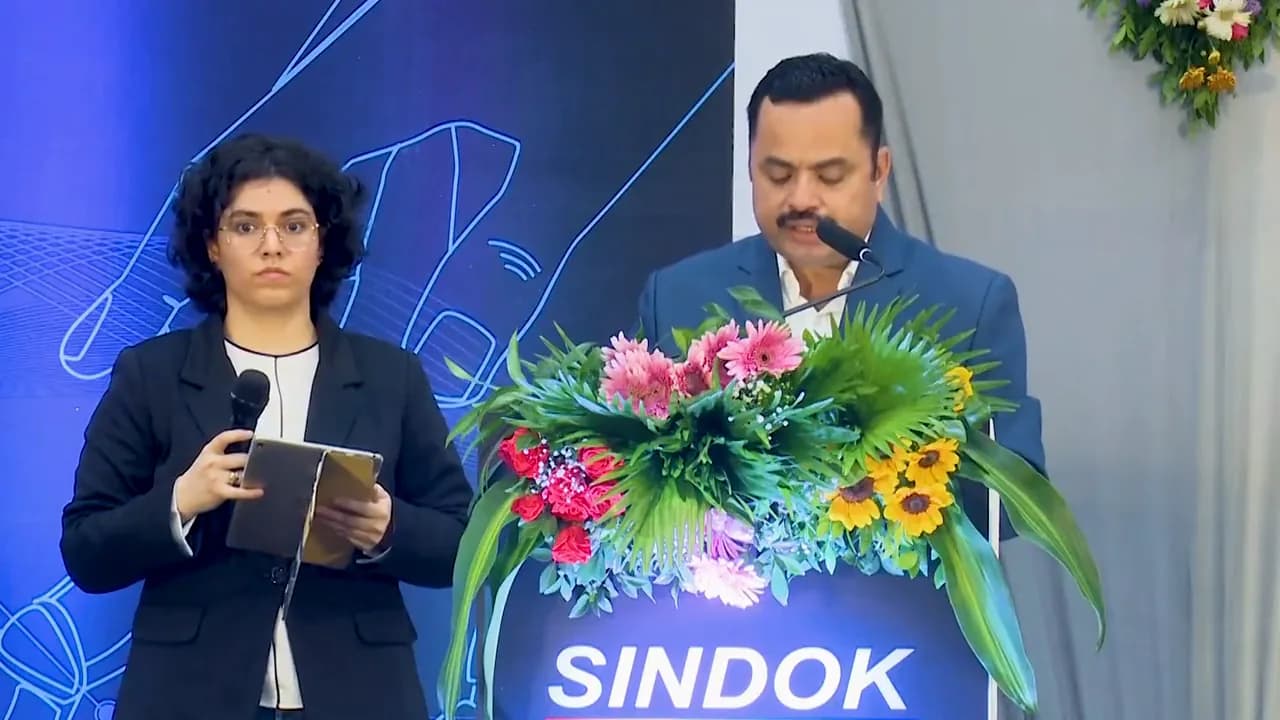 A speaker at a podium against a branded backdrop in blue stage light, a seated audience, and awards handed over on stage.